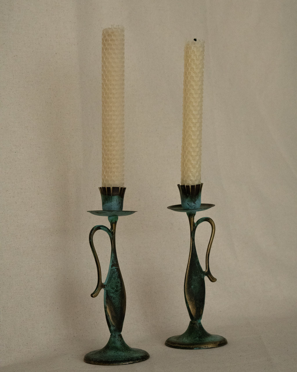 Pair of brass intentional verdigris single candle holders in the shape of vessels with handles