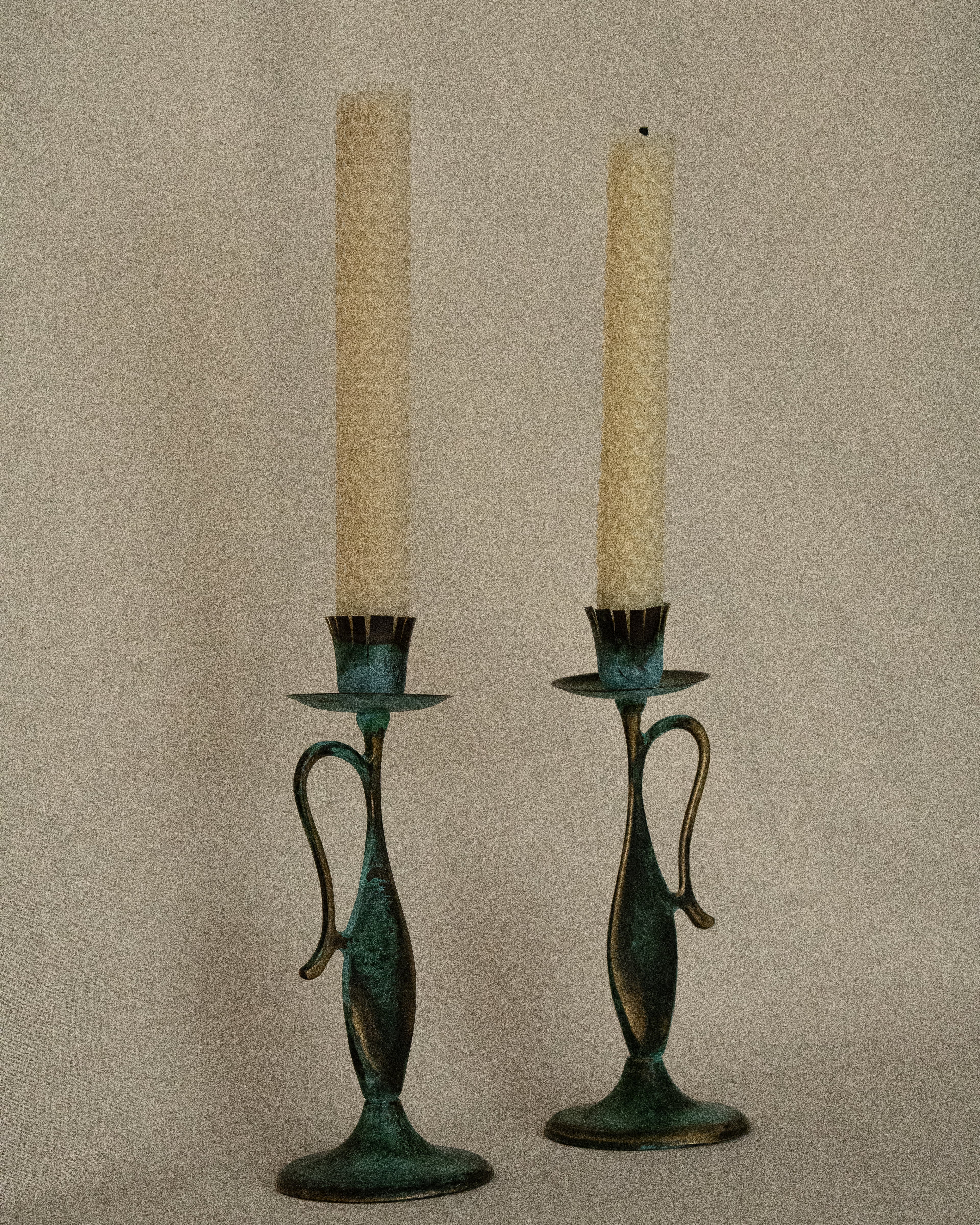 Pair of brass intentional verdigris single candle holders in the shape of vessels with handles