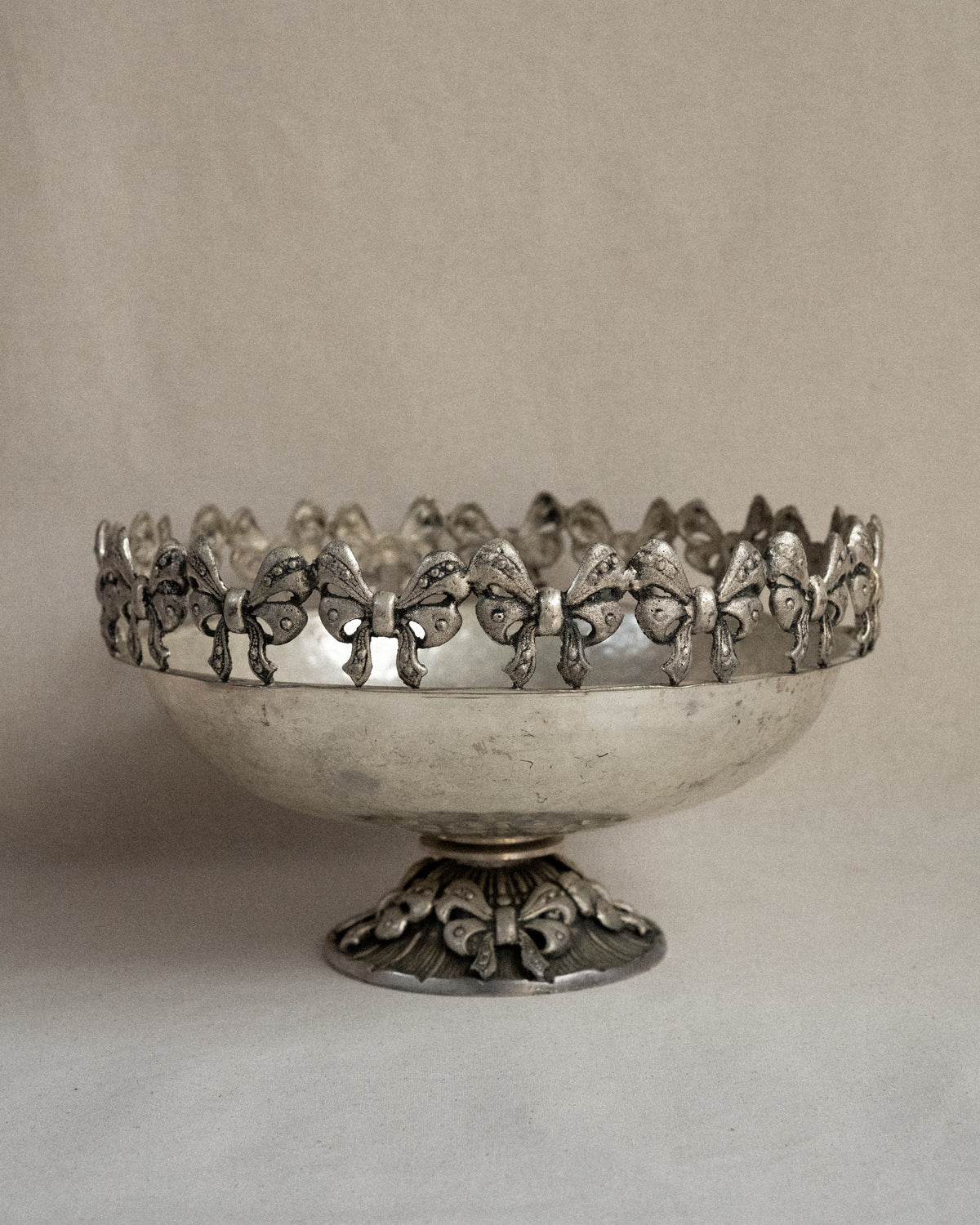 Metal raised bowl with bow details in silver-brass finish