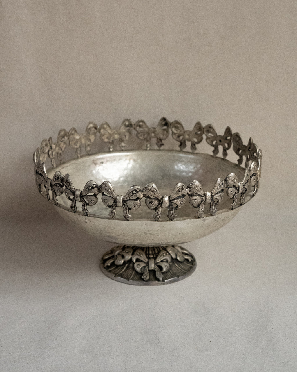 Metal raised bowl with bow details in silver-brass finish