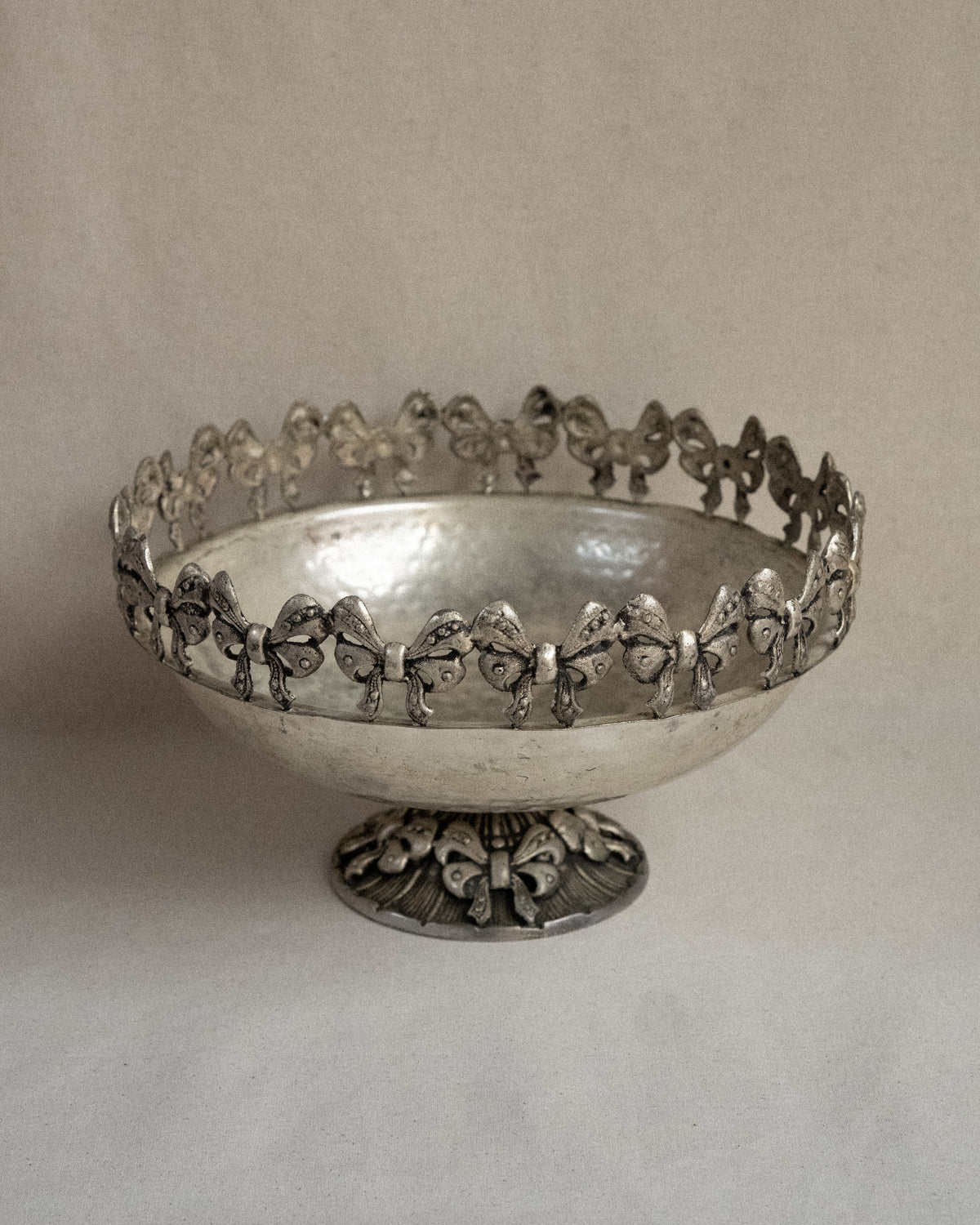 Metal raised bowl with bow details in silver-brass finish