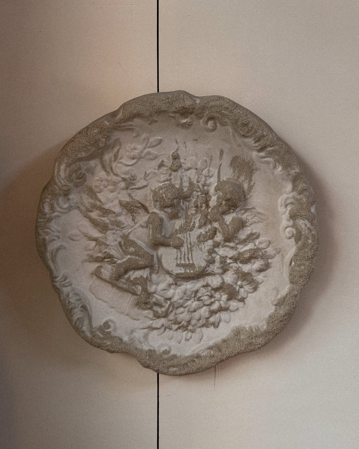 Concrete wall hanging of cherubs playing a lyre harp